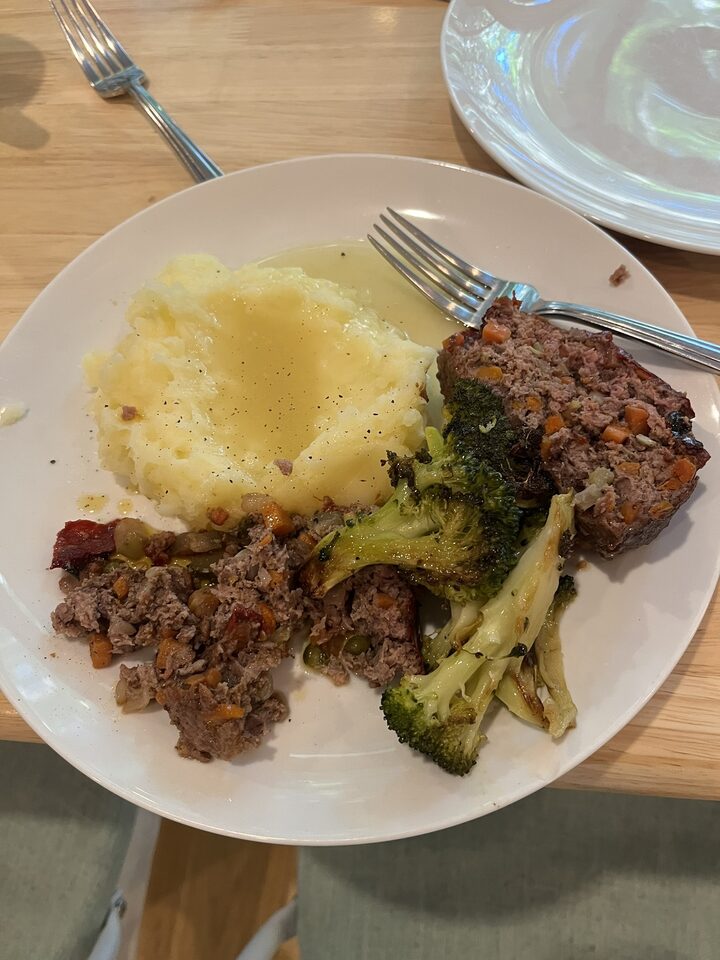 Meatloaf plate with mashed potatoes, gravy, roasted broccoli, one clean slice, and one crumbled slice