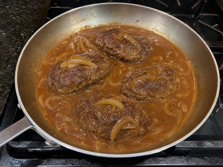 Salisbury steak patties simmering in onion gravy in a skillet